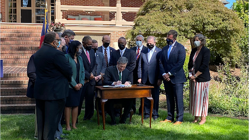 Governor Cooper seated at a desk with members of state legislature around them signing bipartisan climate legislation.