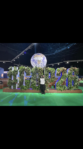 Sophia in front of a sign saying "#COP26" covered in vines with a large globe in the back