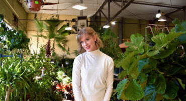 Hannah Rogers dressed in a white turtleneck sweater is pictured surrounded by plants.