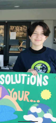 Tula holding up a sign saying "solutions" in large letters with an image of the globe, the sun, and other images. 